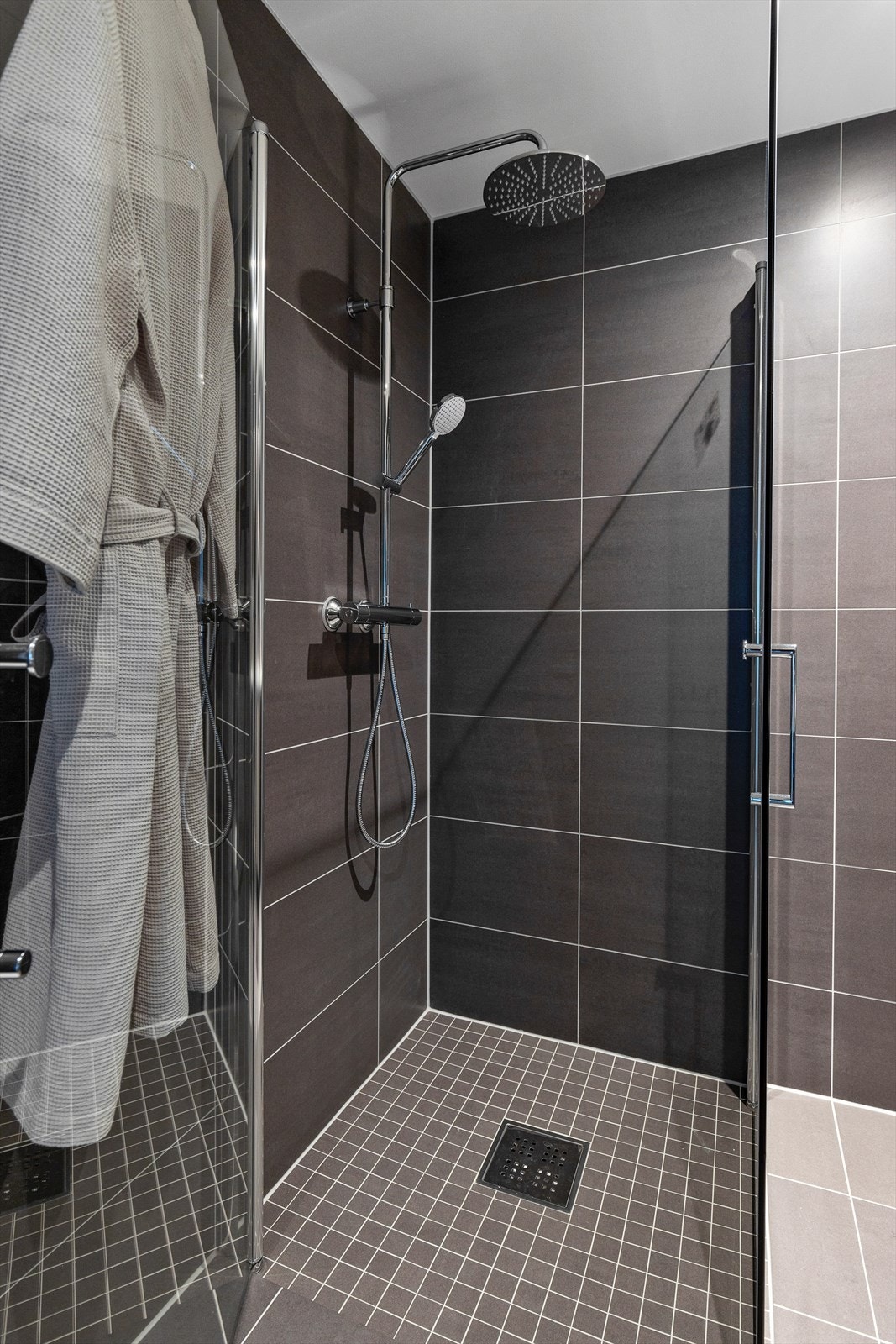 Nedfliset dusjhjørne med glassdører og vegghengt dusjarmatur med regndusj og hånddusj. Galleribilde