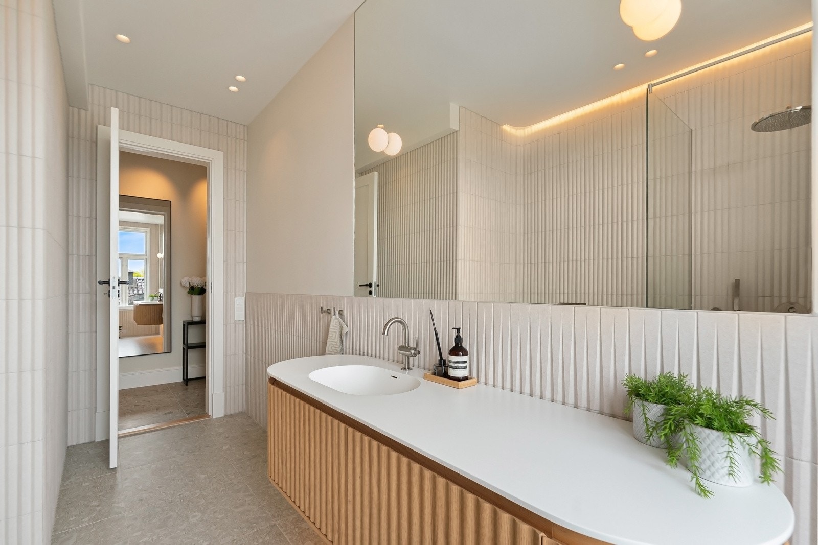 Nydelig gjestebad med adkomst fra hallen, med flotte, buede vegger og overflater kledd i lyse, italienske fliser med rillet tekstur.