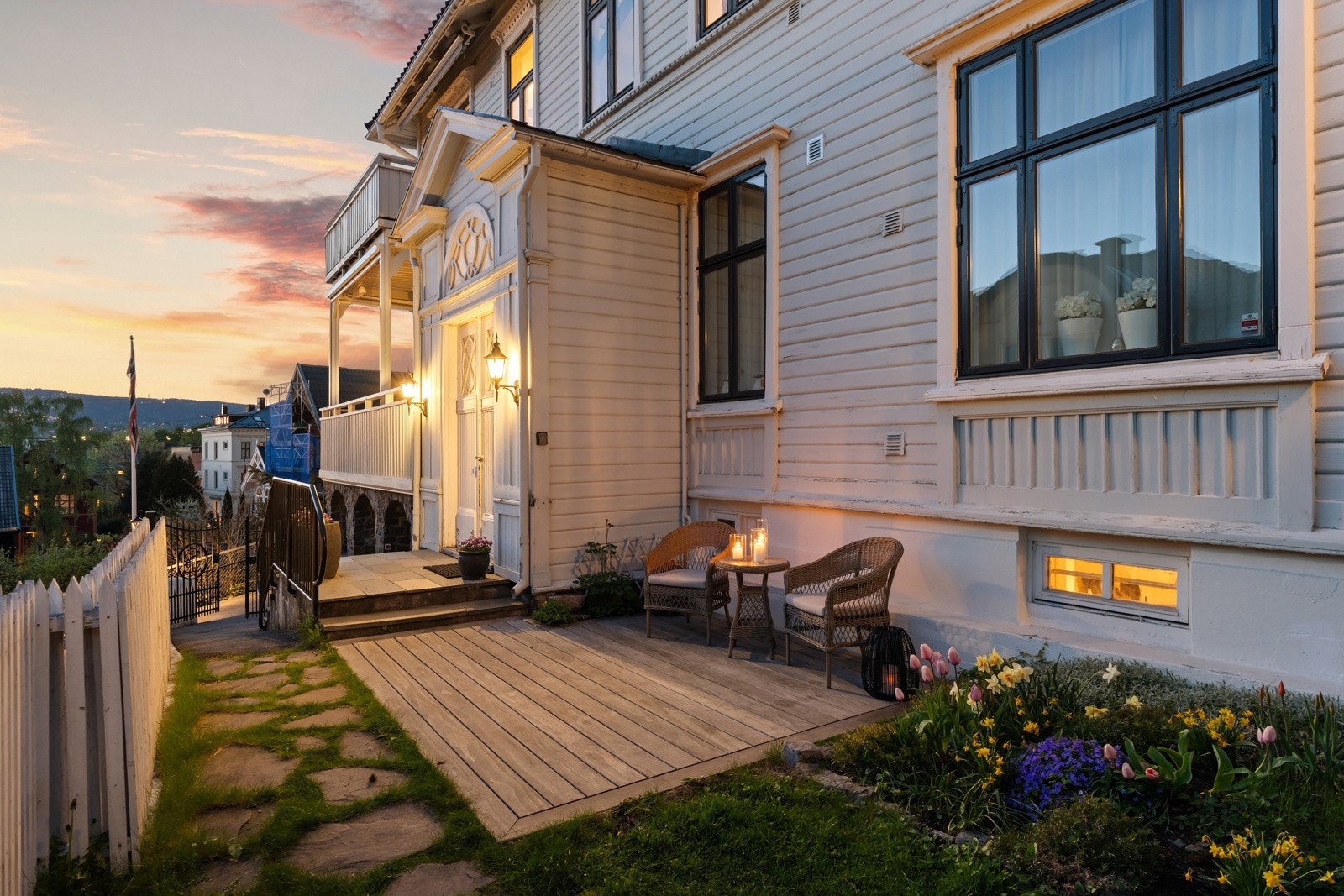 Hagen er grønn og usjenert med gressplen, rammet inn av hvitmalt stakitt, lubne busker og trær i tomtegrensen.