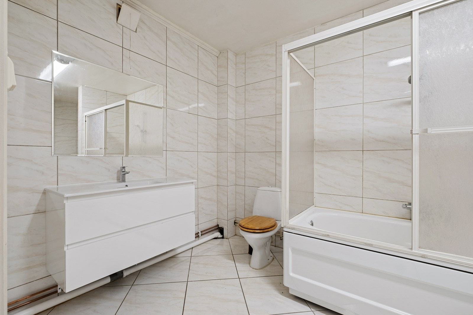 Flislagt baderom med heldekkende servant med underskuffer, toalett og dusj i badekar. Galleribilde