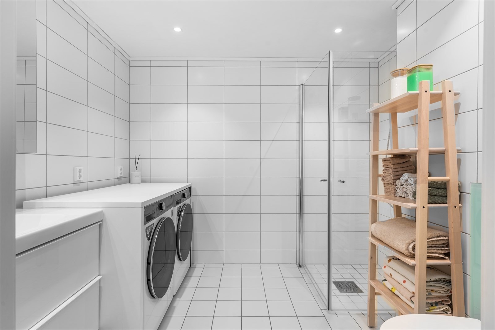 Badet har flislagte overflater, nedsenket dusjhjørne med glassdører og opplegg for vaskemaskin. Galleribilde