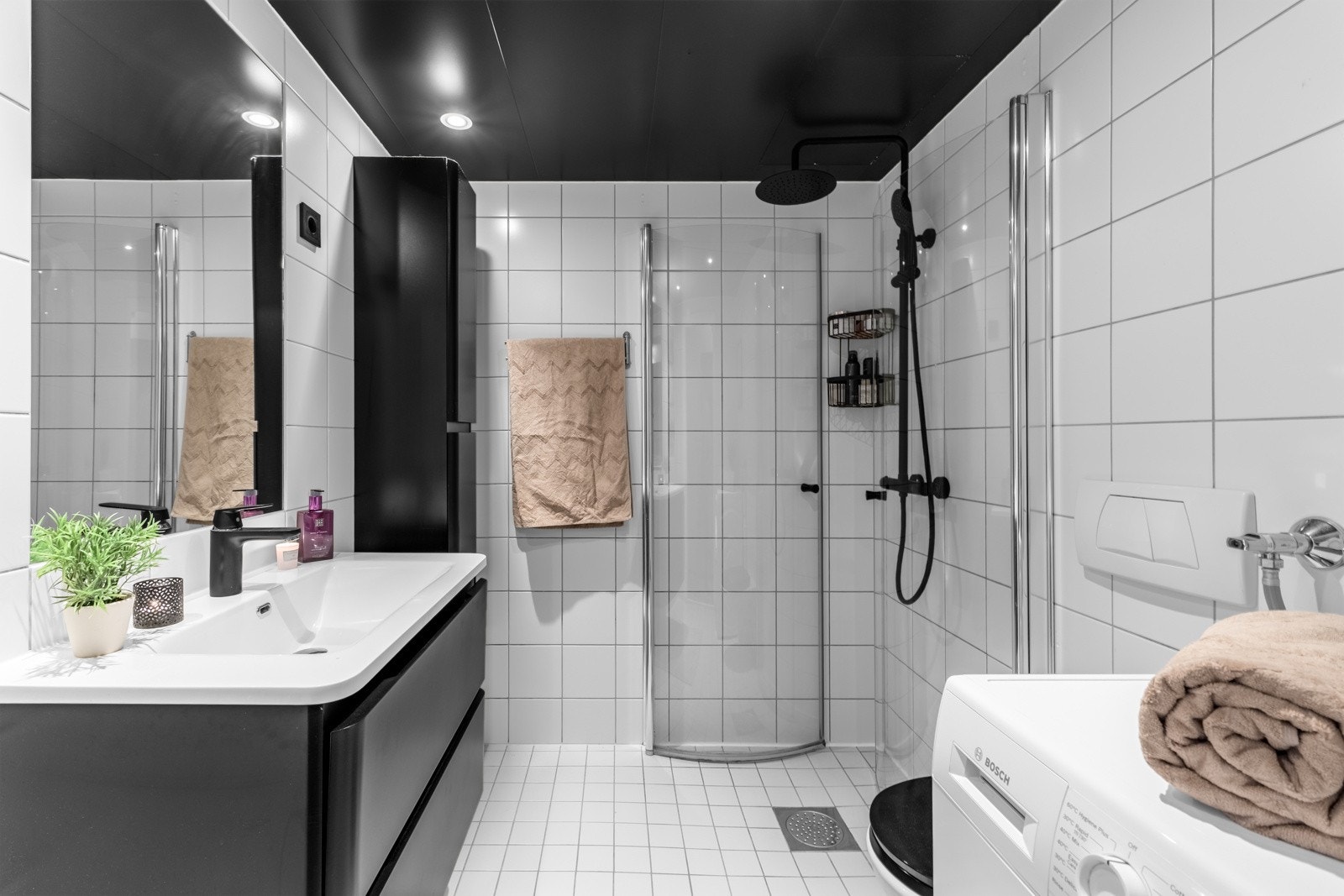 Badet har en moderne utførelse med hvite fliser på gulv og vegger, og kontrastgivende sorte detaljer. Galleribilde