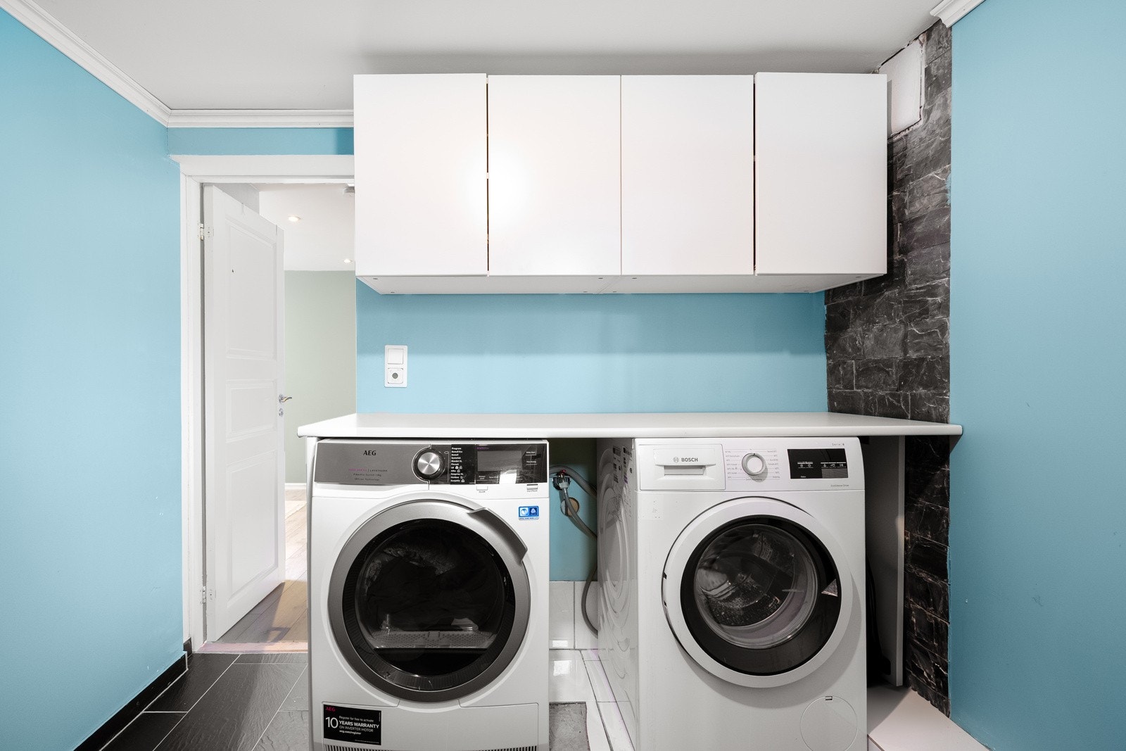 Boligen har et praktisk og innbydende vaskerom i kjelleren, med flislagt gulv og behagelig gulvvarme for ekstra komfort. Veggene er malt i lyse toner, noe som gir rommet et rent og luftig preg. Galleribilde