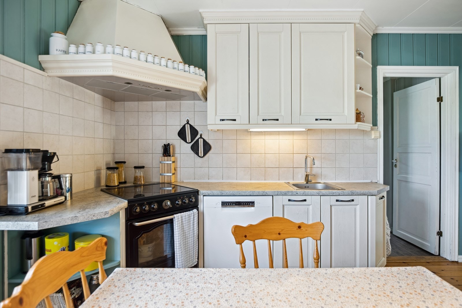 Fliser over kjøkkenbenk, ventilator, frittstående komfyr og opplegg for oppvaskmaskin. Galleribilde