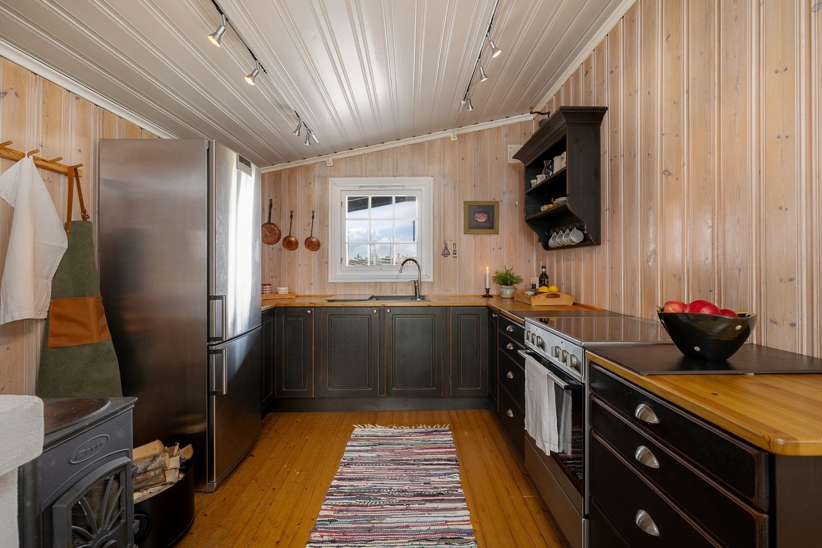 Koselig kjøkken med spiseplass og peis. Innredningen er i svart utførelse med benkeplate i tre. Plass til komfyr og kjøleskap. Galleribilde