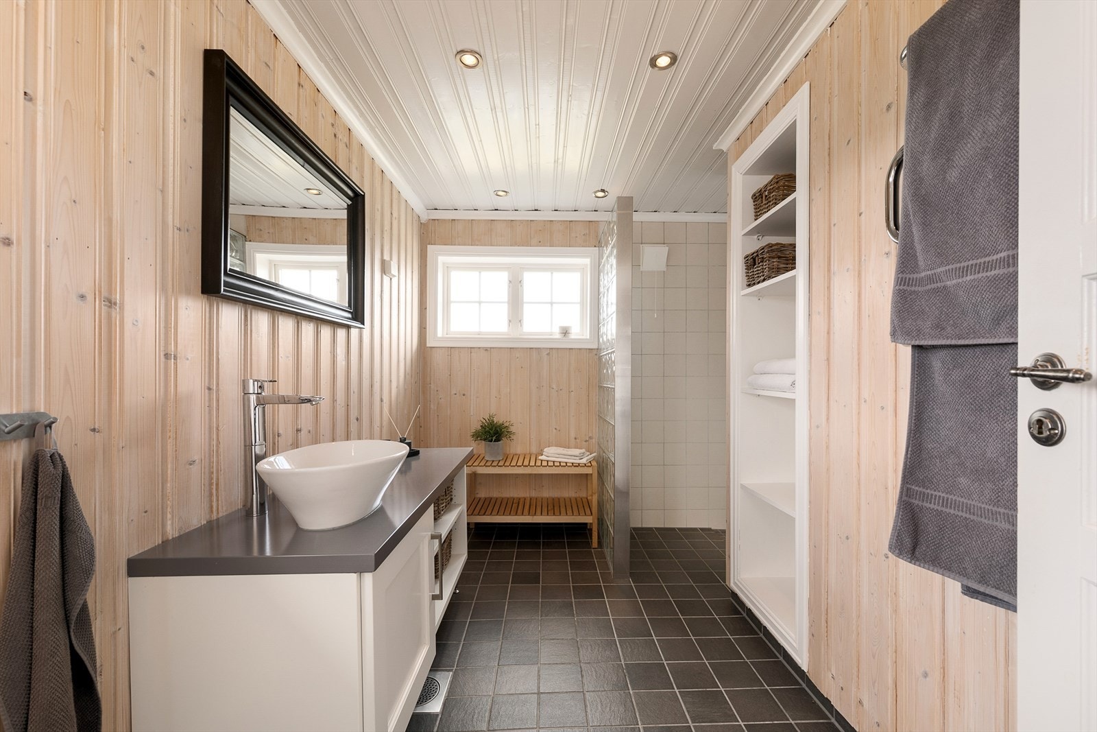 Tidløst og pent bad med fliser på gulv og panel på veggene. Servant med innredning. Spotter i tak. Galleribilde