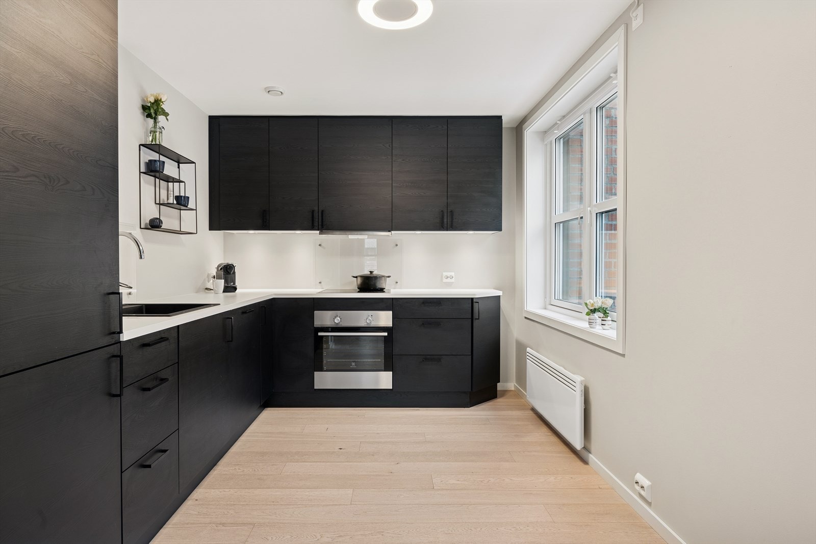 Lekkert sort kjøkken med laminerte fronter og hvit laminert benkeplate. Kjøkkenet er innredet i en praktisk form, med godt med skap og oppbevaringsplass. Galleribilde