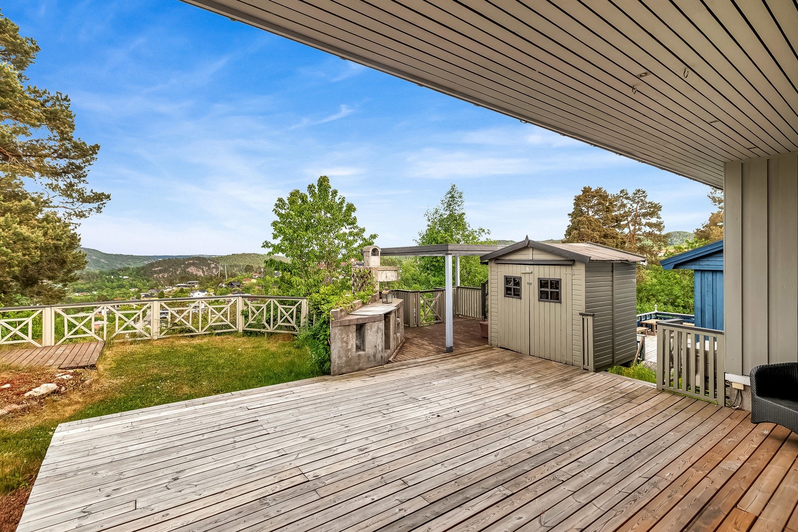 Romslig platting utenfor stuen med frittstående bod og murt utepeis. Galleribilde