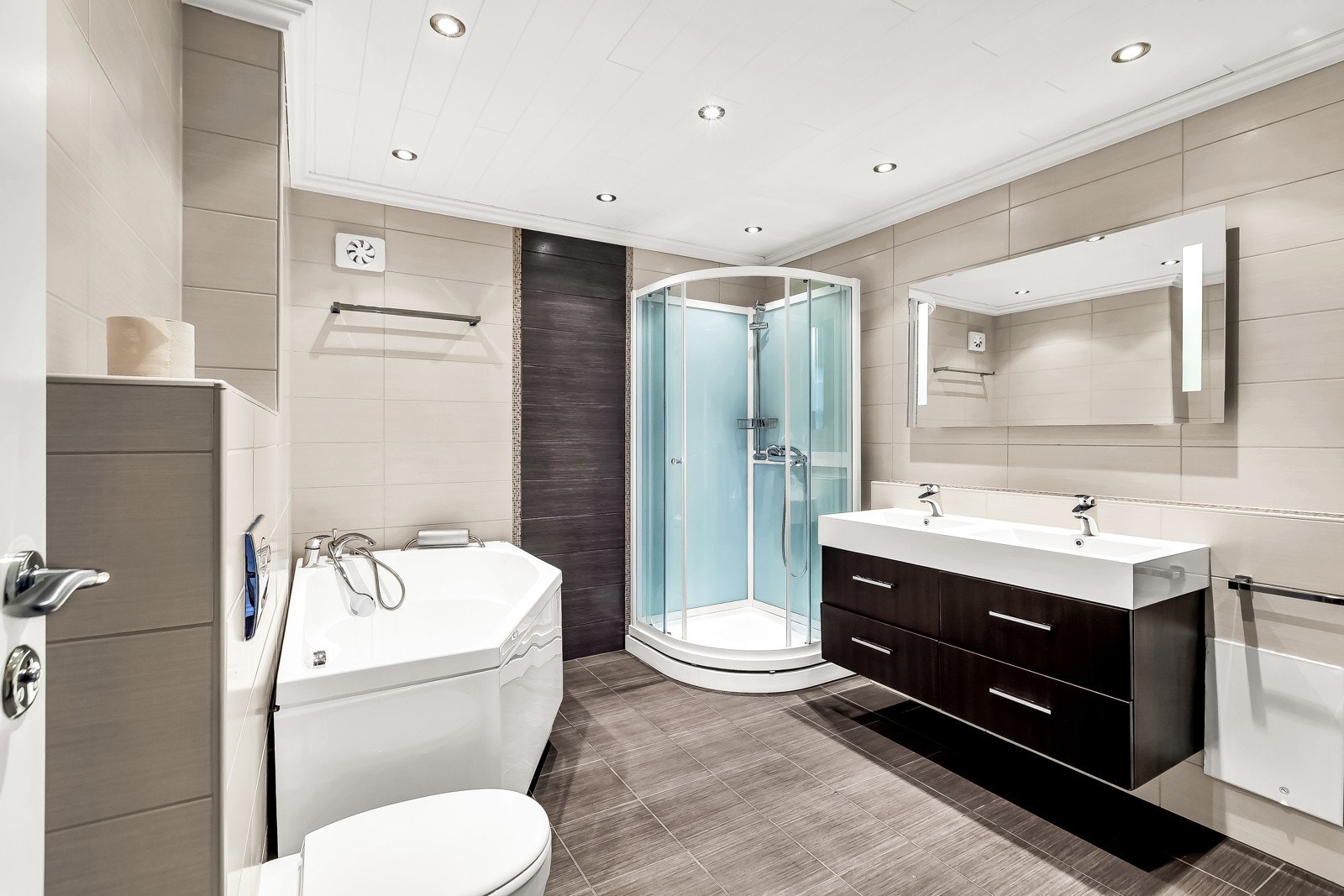 Lekkert flislagt bad fra 2011 i underetasjen. Vegghengt servantinnredning med skuffer og ovenpåliggende servant. Dusjkabinett, badekar, vegghengt toalett og opplegg for vaskemaskin. Galleribilde