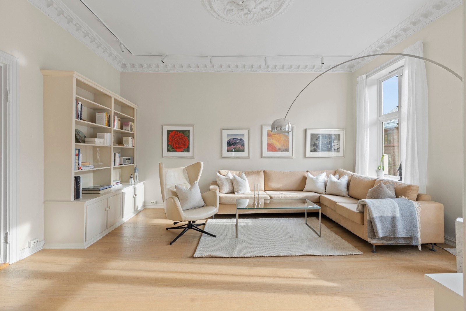 Leilighetens hjerte er den vakre peisestuen. Den imponerende takhøyden på over tre meter og de store vindusflatene slipper inn rikelig med naturlig lys og skaper en luftig og behagelig atmosfære. Galleribilde