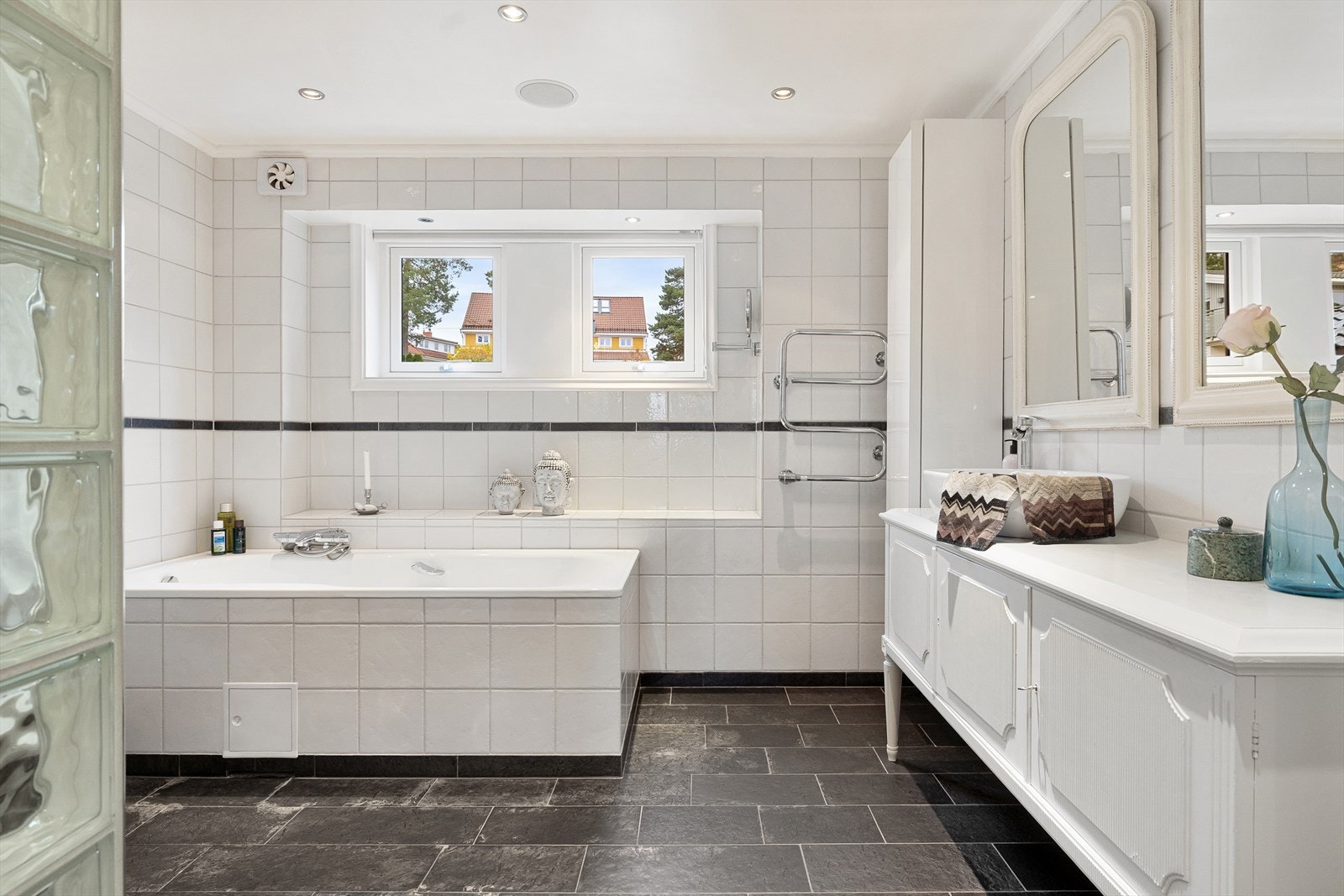 Dette stilrene badet har 20x20 cm fliser på vegger, dimbare spotter som belysning og integrerte høyttalere i taket. Gulvet er belagt med 60x20 cm skiferfliser og har varmekabler. Galleribilde