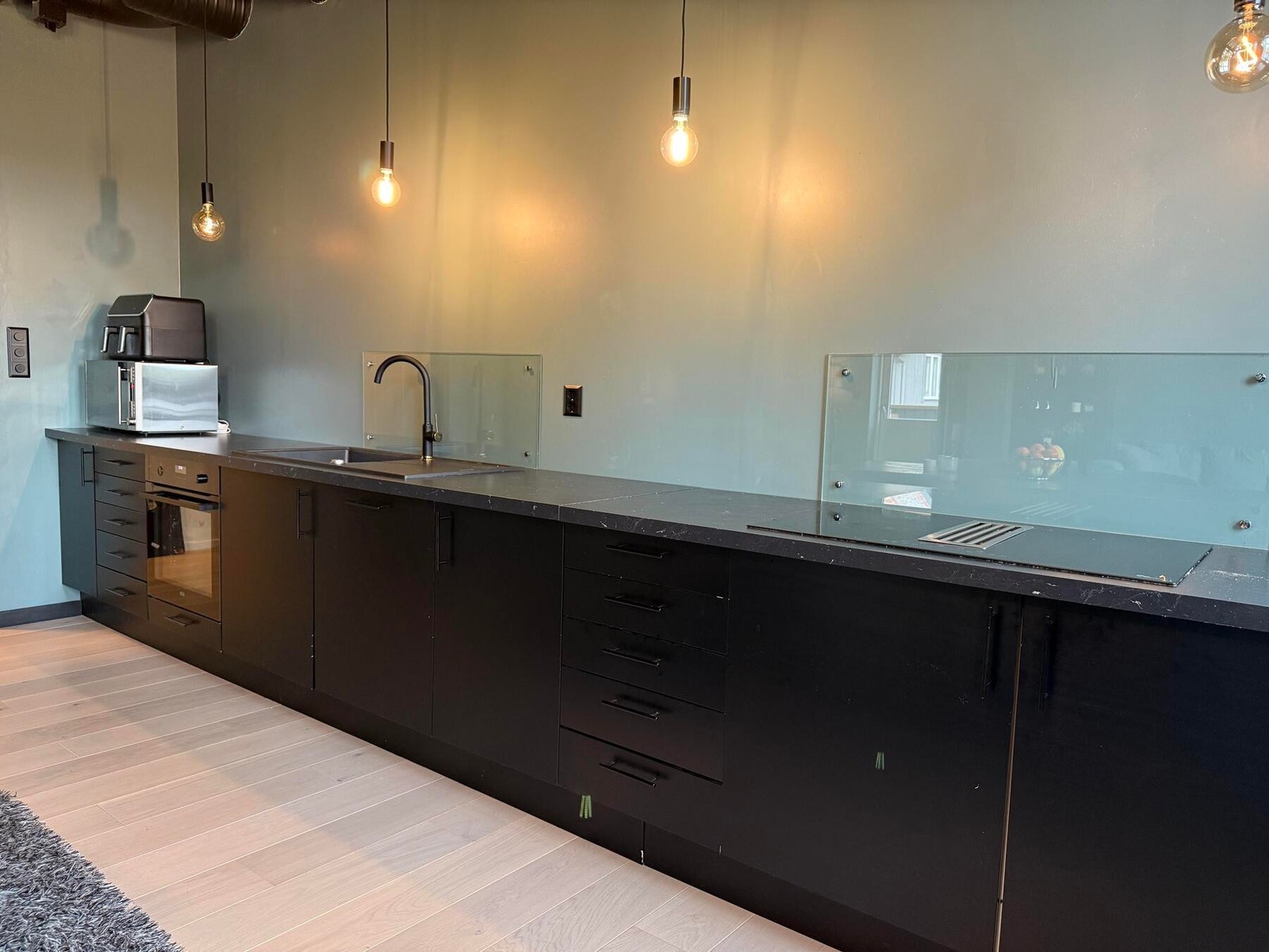 Kjøkken med ventilator i komfyrtopp og glassplate bak platetopp og vask for enkel rengjøring. Galleribilde