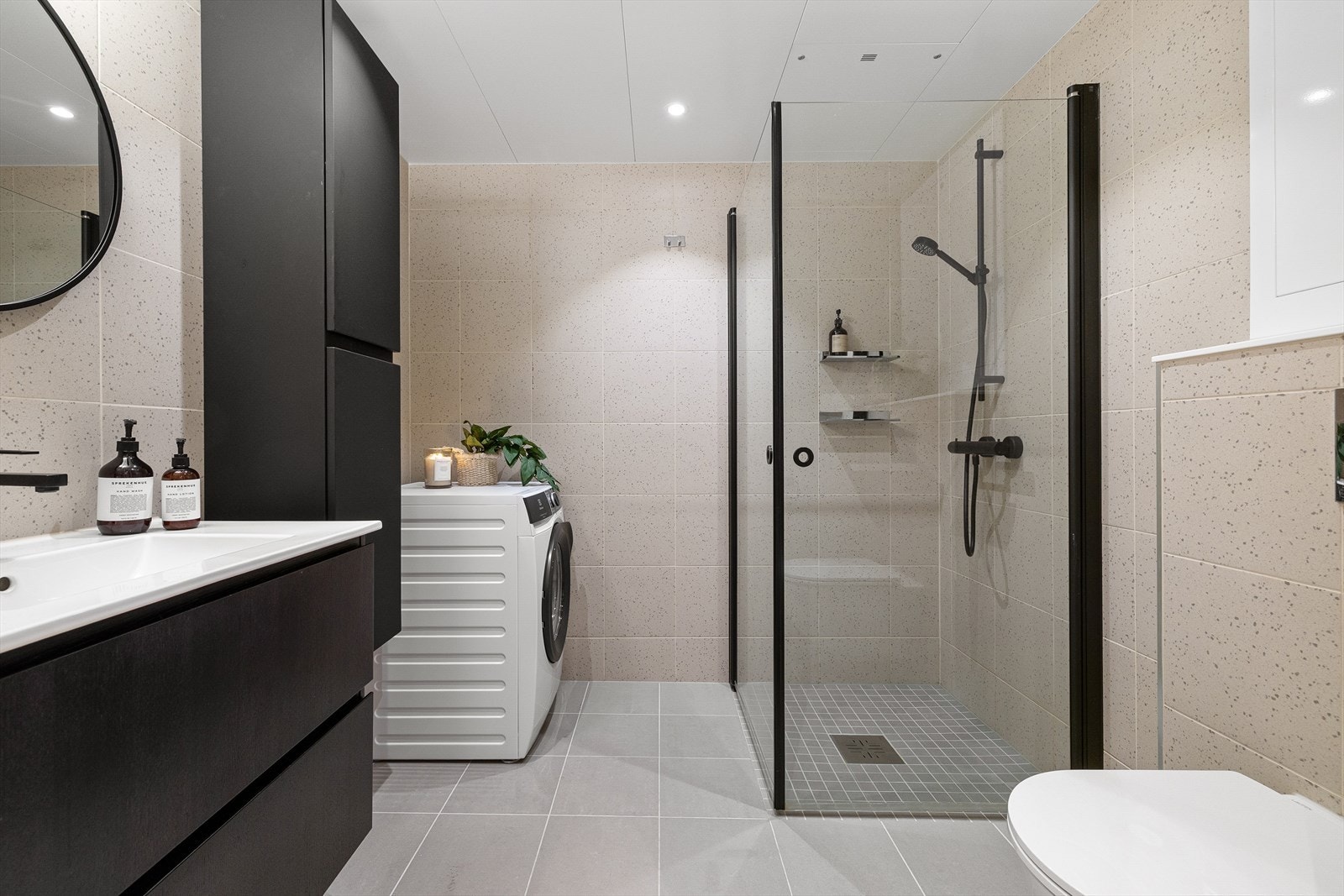 Lekkert lyst flislagt bad med sorte detaljer. Opplegg til vaskemaskin. Galleribilde