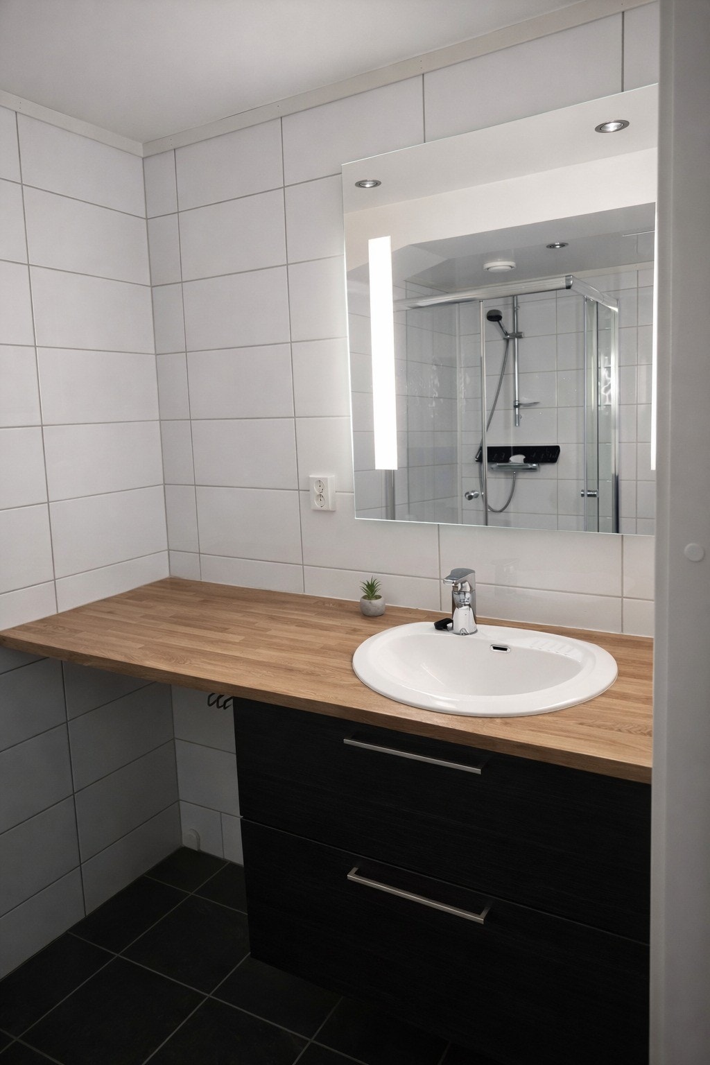 Leiligheten har et romslig, flislagt bad med gulvvarme, servant med underskap og speil med belysning Galleribilde