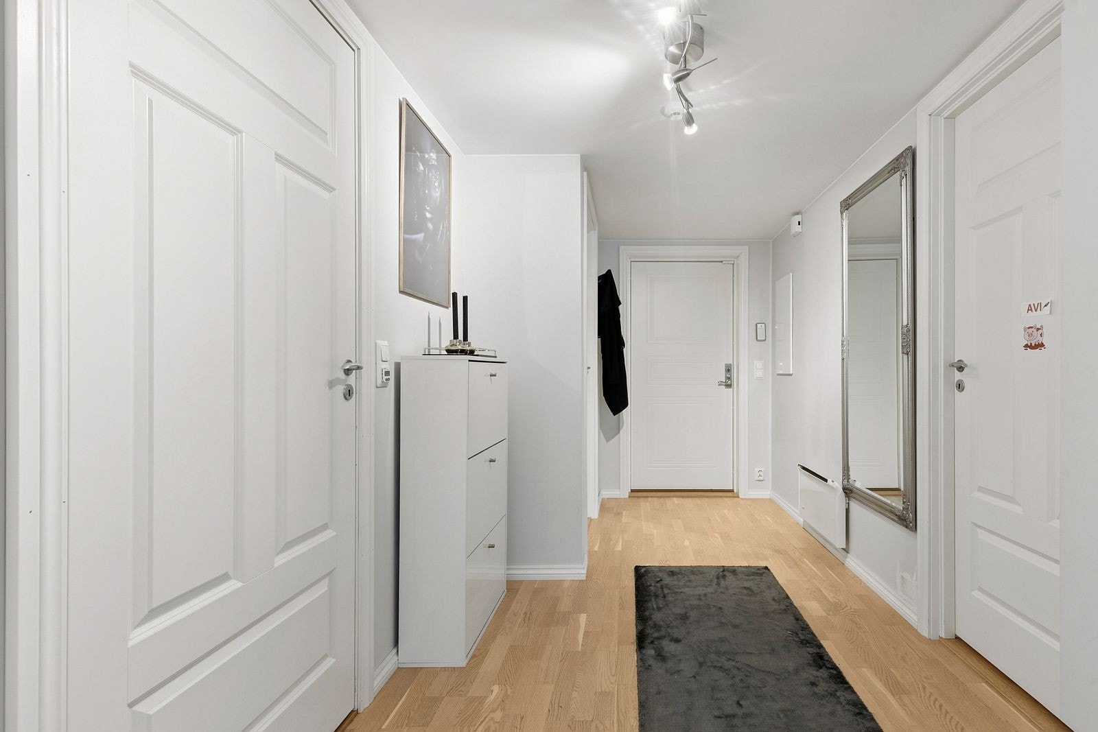 Velkommen inn i en lys entré med parkettgulv som leder videre inn i leiligheten. Galleribilde