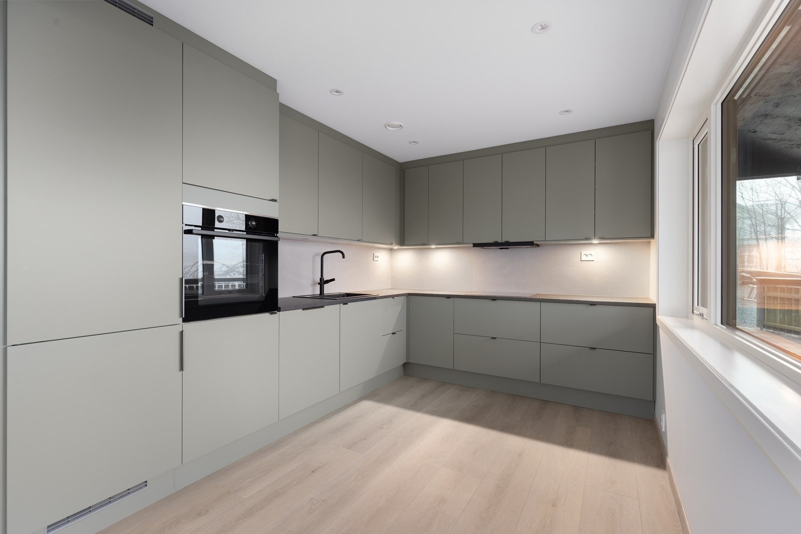 Kjøkkendelen har en stilren og moderne innredning med grønne slette fronter, sort laminert benkeplate med steinimitasjon og sort nedfelt kum, samt flis over kjøkkenbenk. Galleribilde