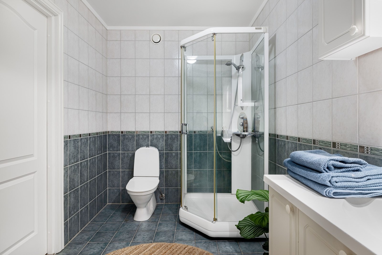 Lys baderomsinnredning med nedfelt servant, speil med belysning og vegghengte skap over. Baderommet er også utstyrt med dusjkabinett og gulvstående toalett. Galleribilde