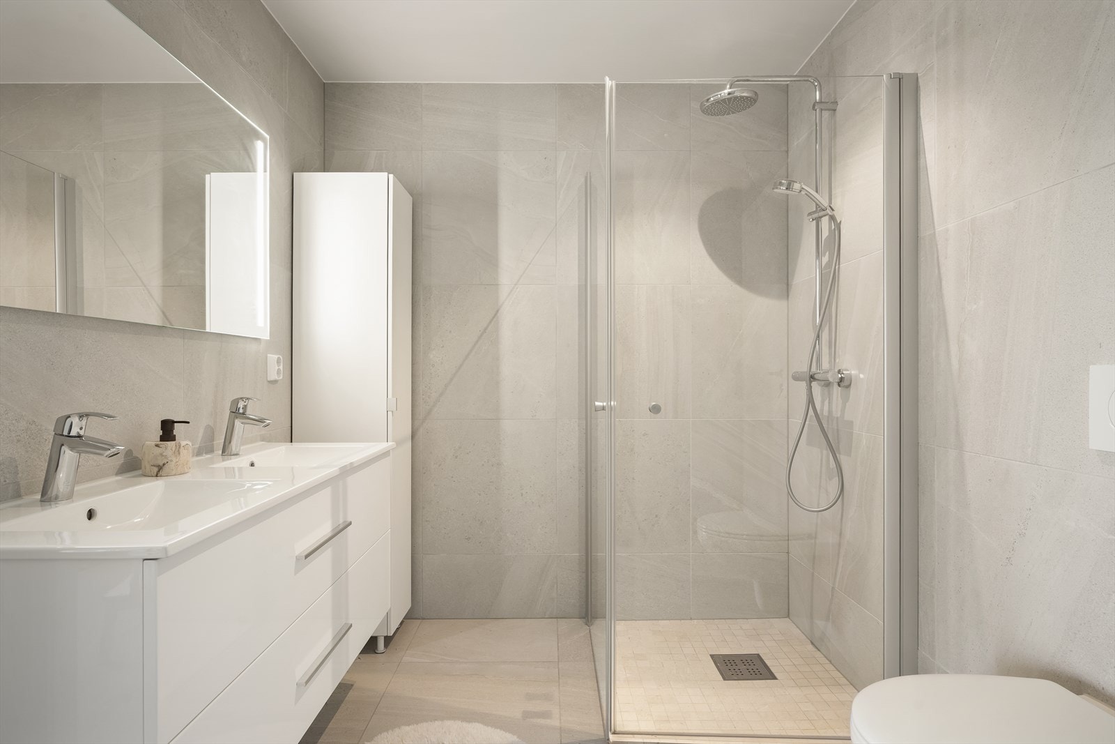 Moderne bad med dobbel servant, speil med integrert belysning og praktisk oppbevaring.
Videre utstyrt med veggehengt toalett og dusjsone med glassvegger. Galleribilde