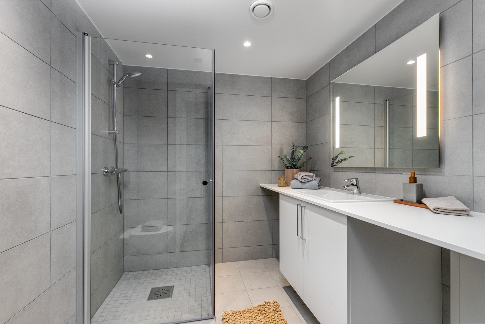 Delikat flislagt bad med vegghengt toalett, dusjsone med innfellbare dører samt servant med skapinnredning. Bilde fra leilighet L104. Galleribilde