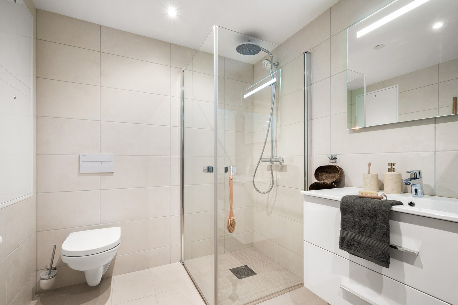 Badet inneholder vegghengt toalett, helstøpt servant, skuffer under servant med slette fronter, dusjdører i klart glass. Galleribilde