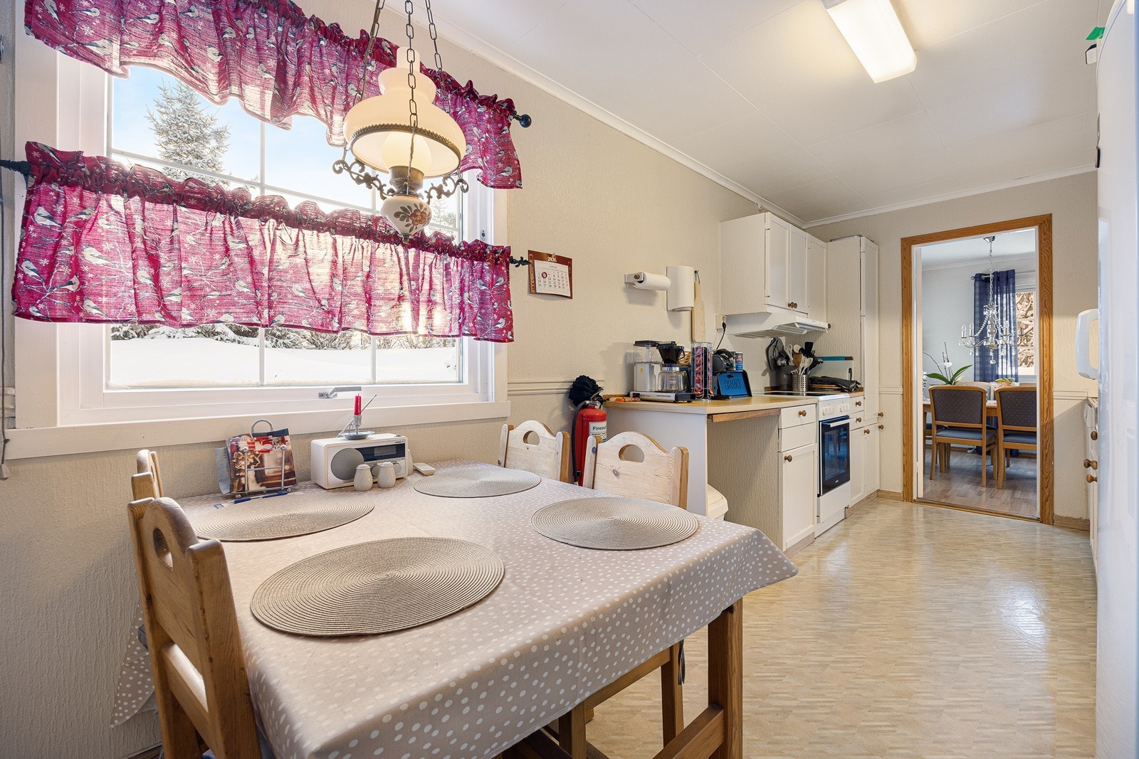 Belysning er montert over benken, og over kokesonen har kjøkkenet en ventilator med avtrekk. Hvitevarene består av komfyr, kjøleskap og oppvaskmaskin. Galleribilde