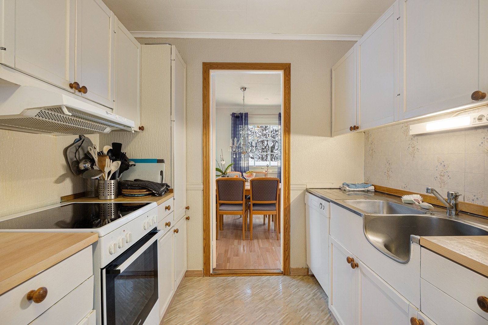 Kjøkkeninnredningen består av to parallelle seksjoner, med hvite, profilerte fronter, benkeplate av laminat og dobbel oppvaskkum i metall. Galleribilde