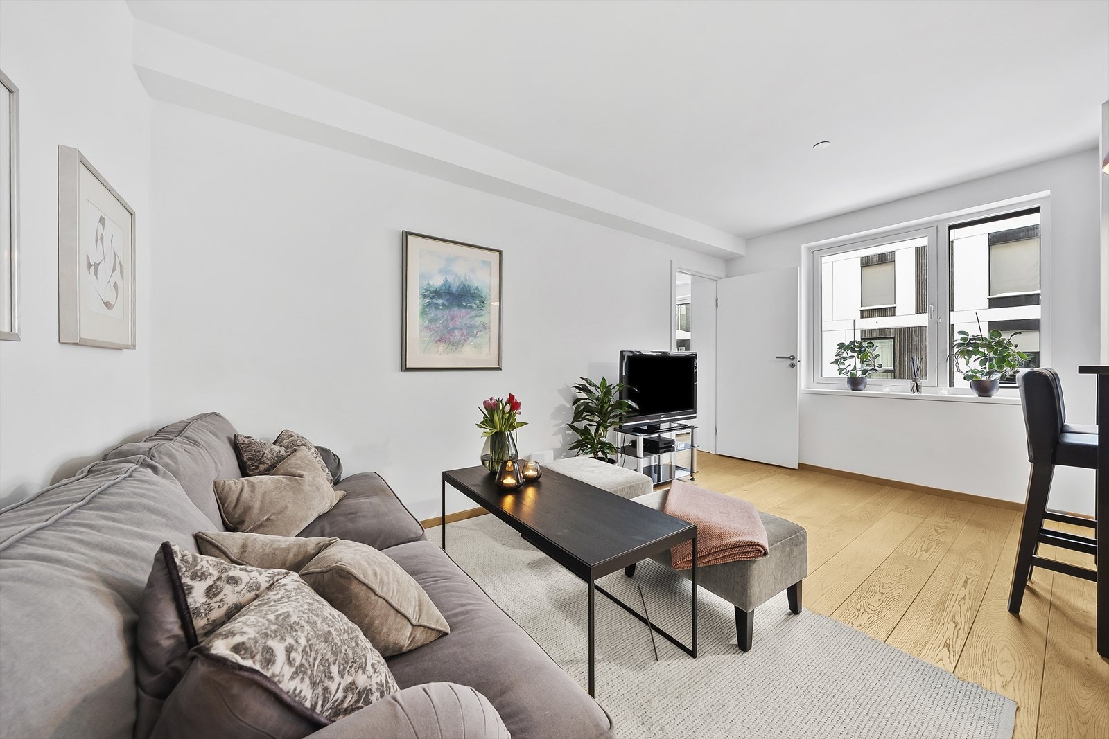 Stilren stue med moderne og lyse farger på vegger og et pent tregulv. Vindusrekke langs med rommet, er med på å slippe inn godt med naturlig sollys. Galleribilde