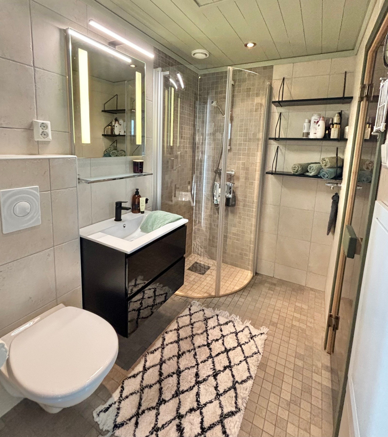 Flislagt bad med gulvvarme. Badet er utstyrt med vegghengt servantinnredning, dusjhjørne med dører og vegghengt dusjarmatur, samt vegghengt toalett. Opplegg for vaskemaskin. Galleribilde