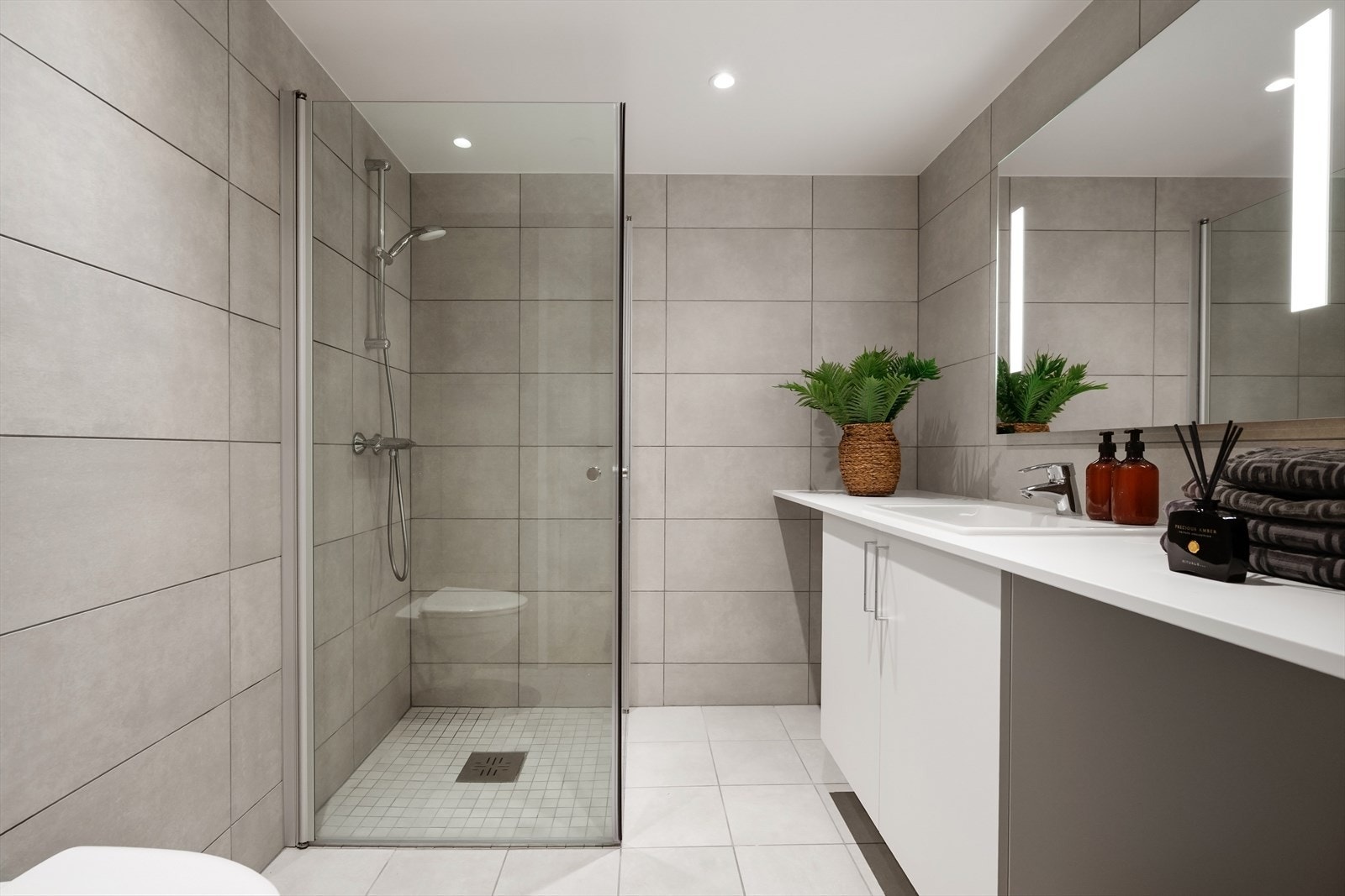 Delikat bad med store fliser, downlights i himling og varmekabler i gulv. Galleribilde