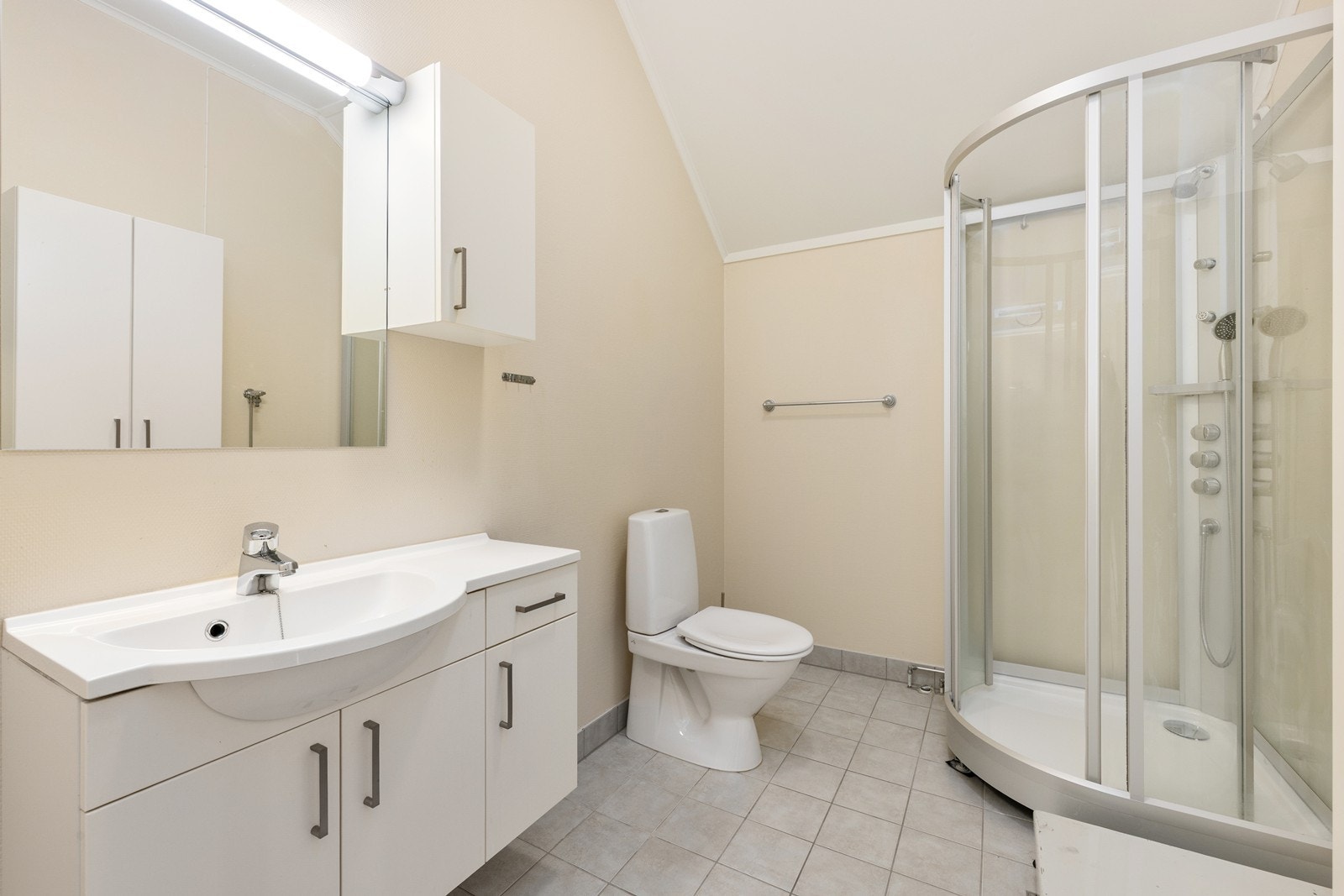 Eldre bad med våtromstapet på vegger og fliser på gulv. Rommet har elektriske varmekabler. Rommet har innredning med nedfelt servant, toalett og dusjkabinett. Opplegg for vaskemaskin. Galleribilde