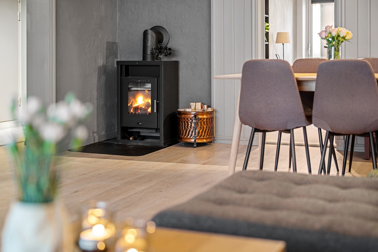 Detaljbilde av vedovn med moderne uttrykk og praktisk plassering i tilknytning til spiseområdet. Nytt røykrør fra 2023. Galleribilde