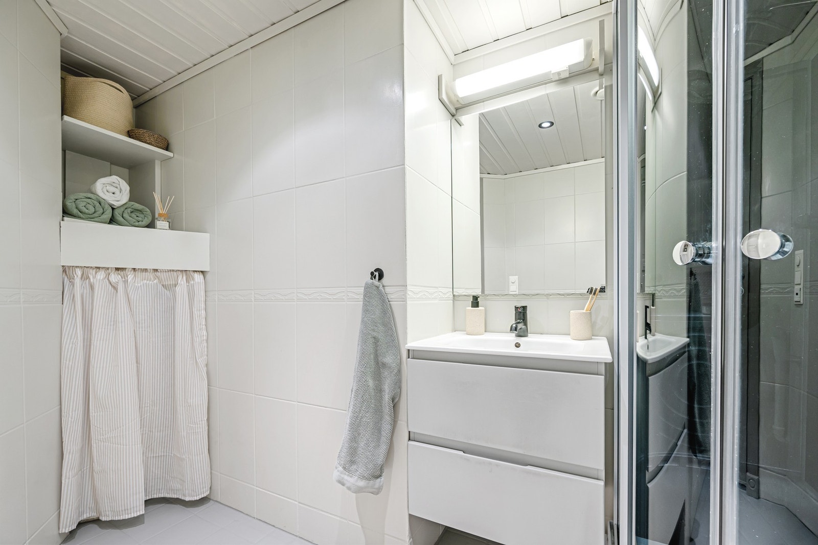 Badet har servantmøbel med god oppbevaringsplass, speil med belysning og praktiske hyller for håndklær og toalettartikler. Galleribilde