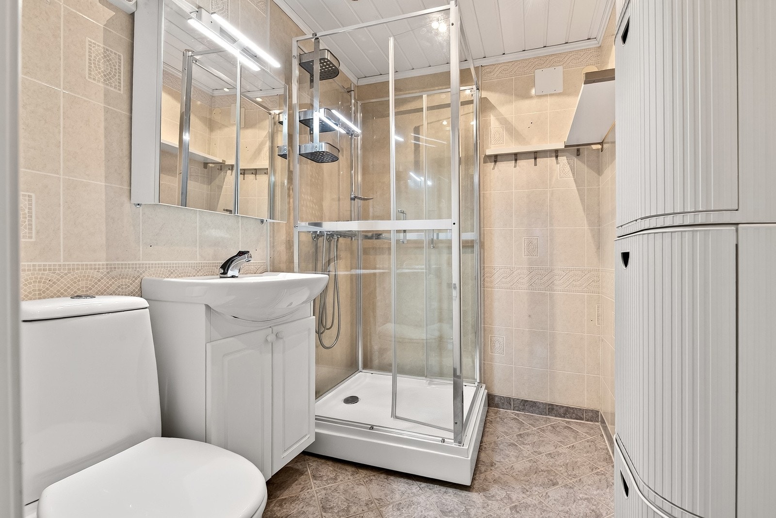 Badet i 1.etg har flislagt gulv og vegger, servantinnredning med skapløsning, speilskap med overliggende lys og dusjkabinett. Galleribilde