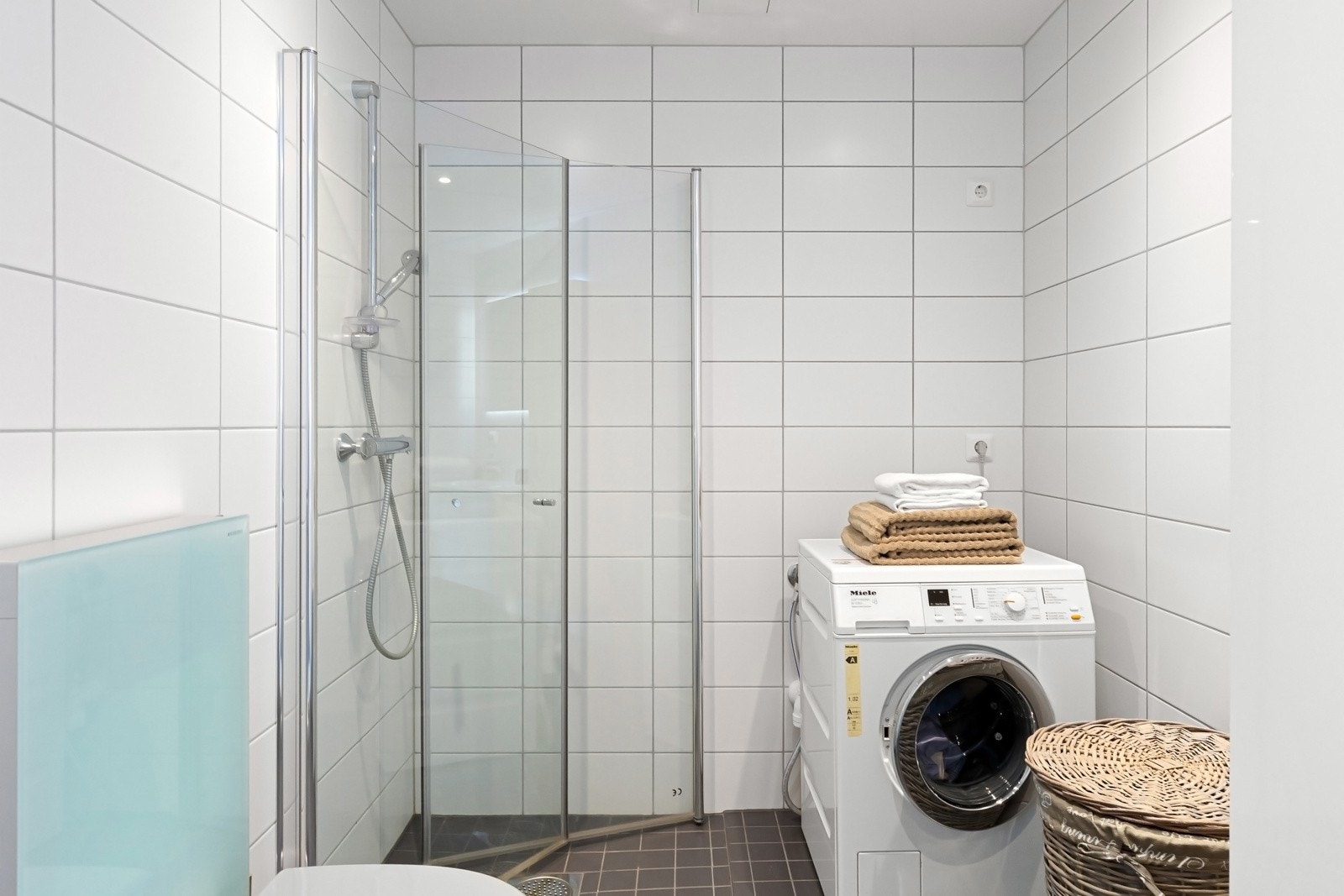 Bad ved soverom er utstyrt med dobbelt servant med slette fronter, veggmontert toalett med utenpåliggende sisterne, dusjhjørne med innfellbare glassdører og opplegg for vaskemaskin Galleribilde