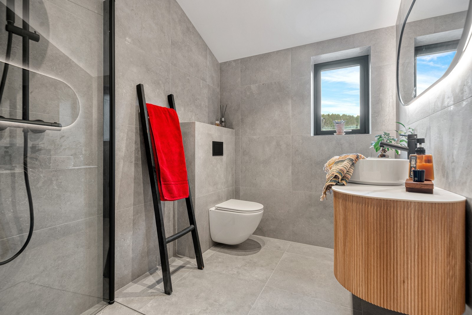 Lekkert baderom bestående av vegghengt toalett, baderomsinnredning og dusjhjørne med glassvegg. Galleribilde