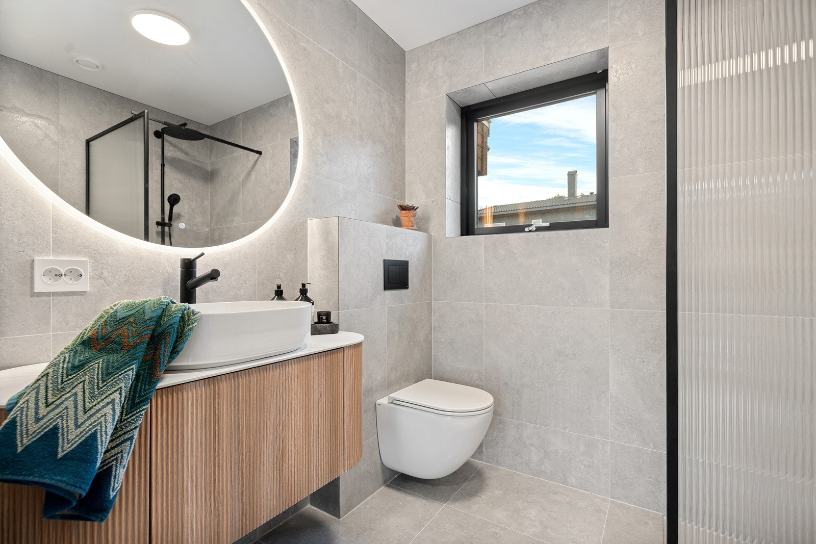 Lekkert baderom bestående av vegghengt toalett, baderomsinnredning og dusjhjørne med glassvegg. Galleribilde