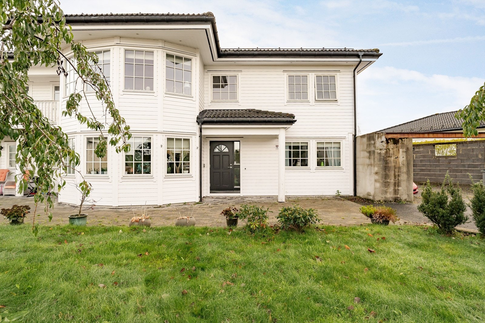 Boligen har en flott fasade med store vinduer som gir rikelig med naturlig lys | Foran huset er det en pent opparbeidet hage Galleribilde