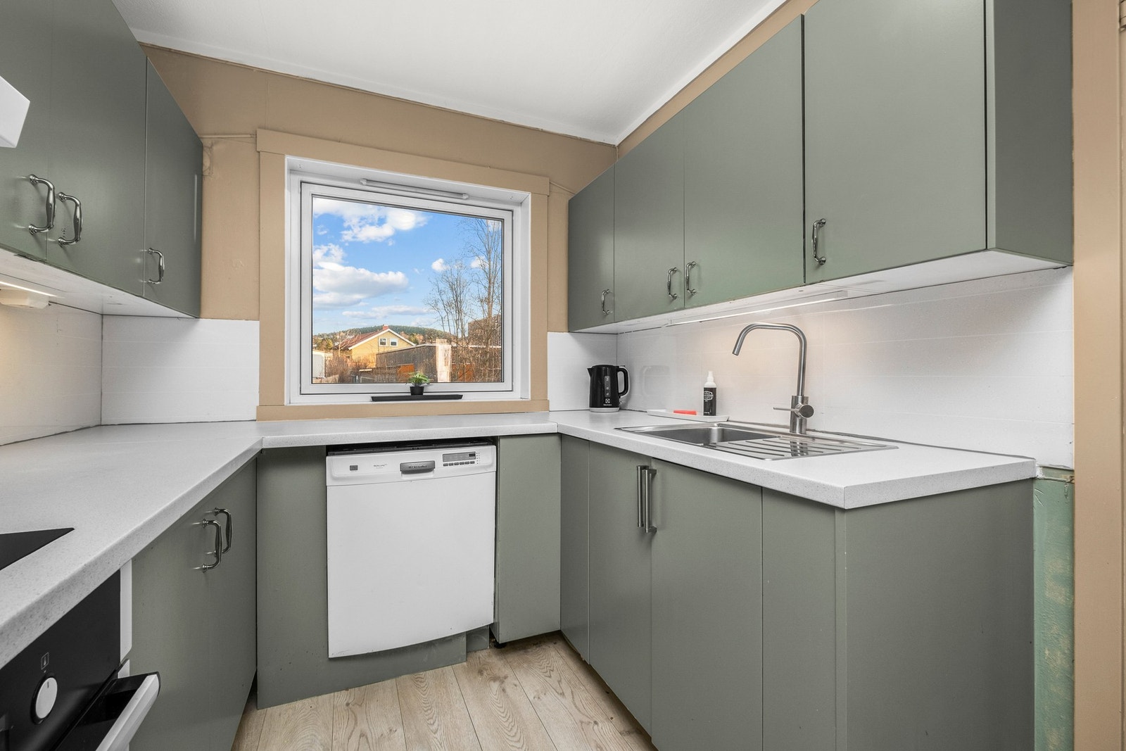 Kjøkkeninnredningen har glatte fronter med integrert stekeovn og frittstående oppvaskmaskin og kjøle/fryseskap Galleribilde