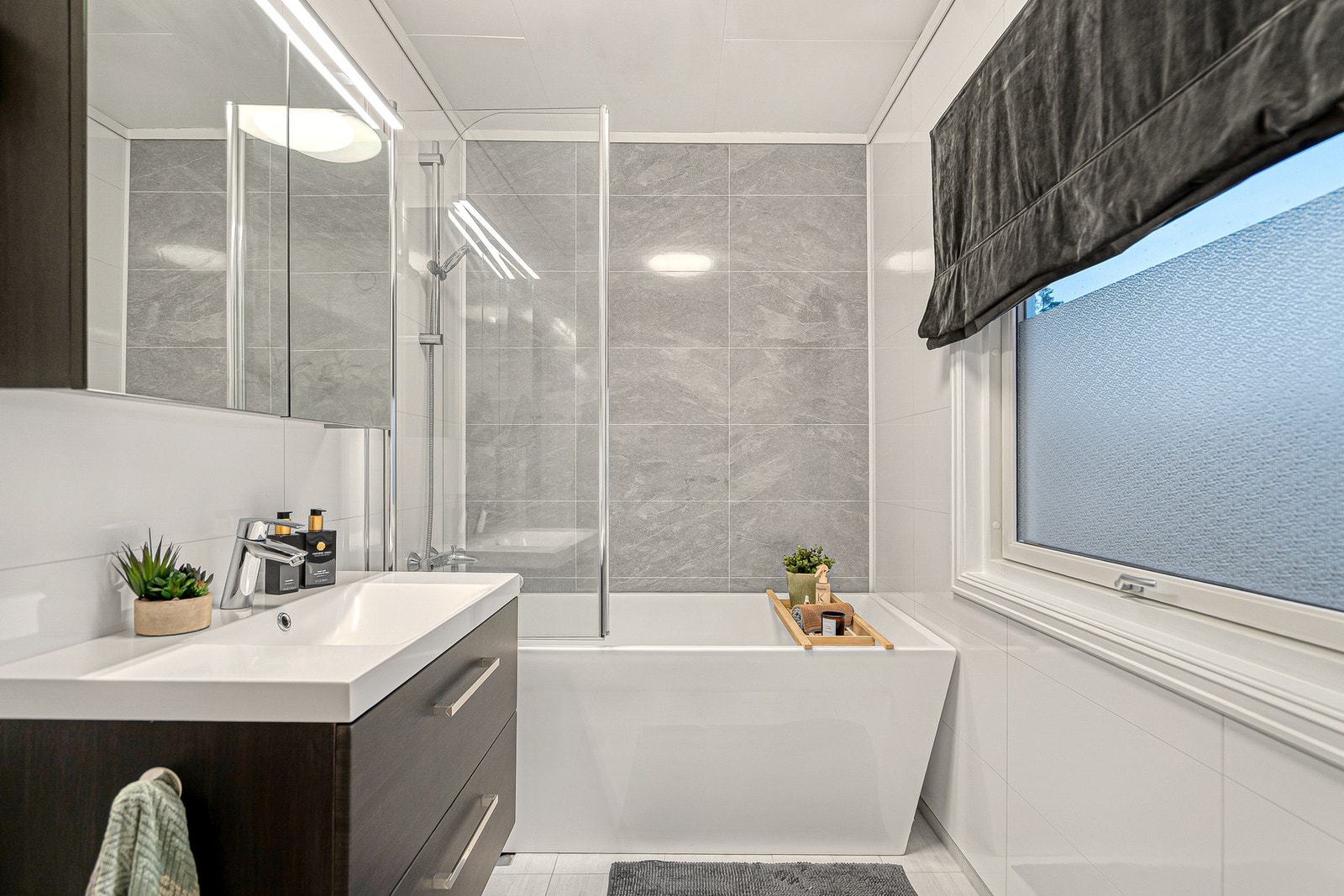 Hovedbadet fremstår tidløst og delikat, med fliser, behagelig gulvvarme, servant med underskap, speilskap og vegghengt toalett. Galleribilde