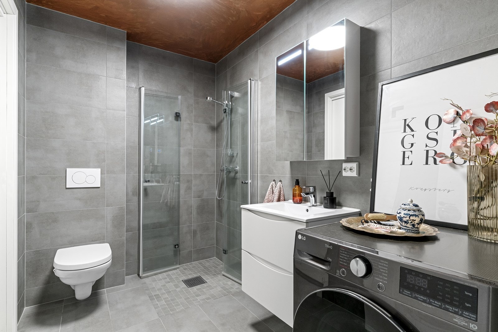 Baderom 1 av 2. Flislagt med gulvvarme. Her finner man også opplegg for vaskemaskin, i tillegg til dusjnisje, toalett og servant med speilskap over. Galleribilde