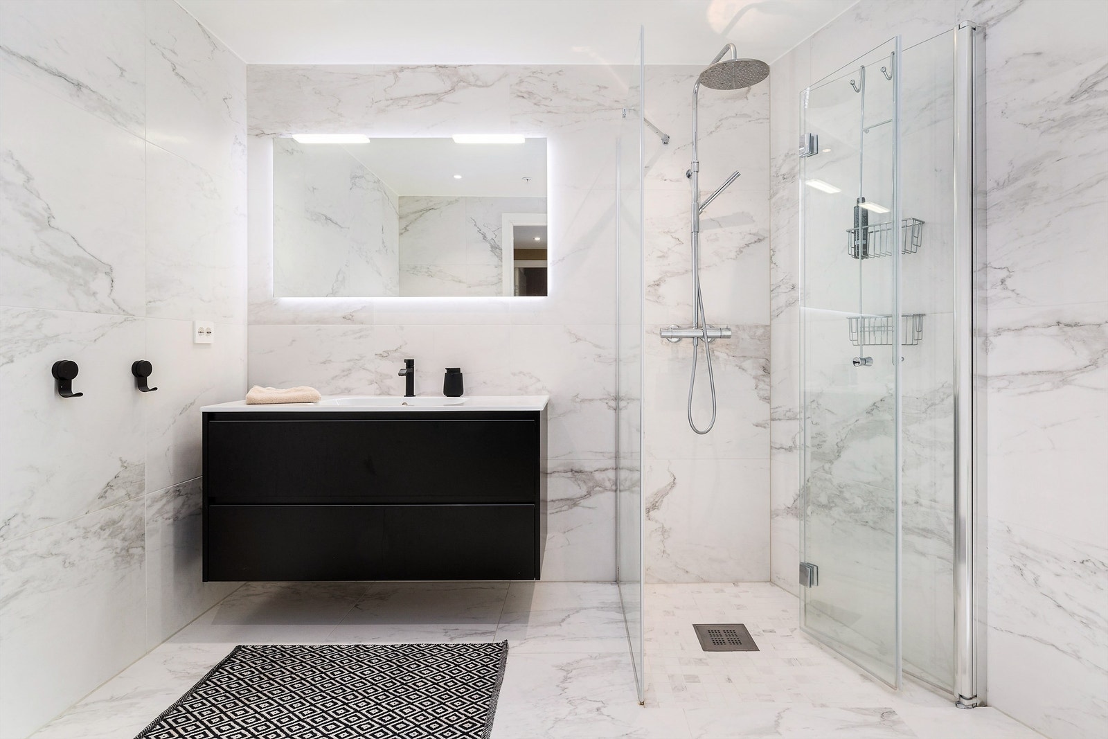 Leilighetens hovedbad er lekkert flislagt med 60x60 Calcatta-fliser fra Stone & More, som gir et luksuriøst og tidløst uttrykk. I dusjsonen er det valgt matchende 5x5 fliser på gulv for et helhetlig inntrykk Galleribilde