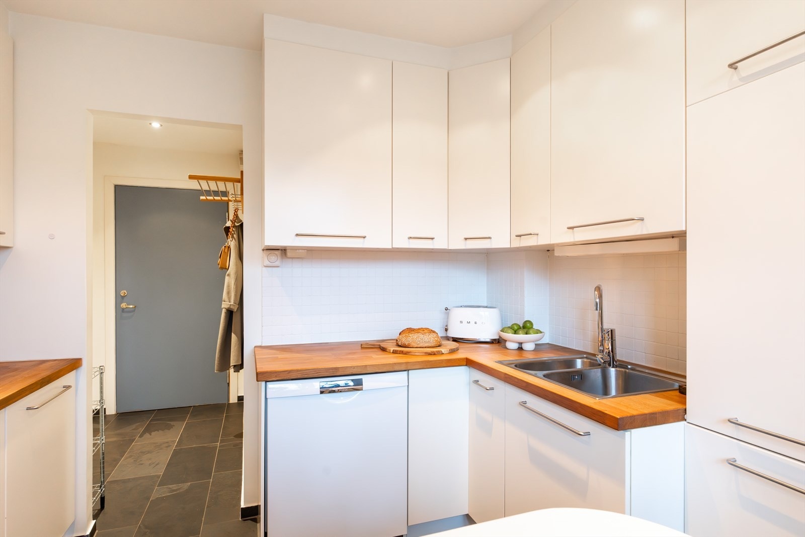 Kjøkkeninnredning bestående av hvite, glatte fronter og benkeplate i heltre med nedfelt vask. Galleribilde