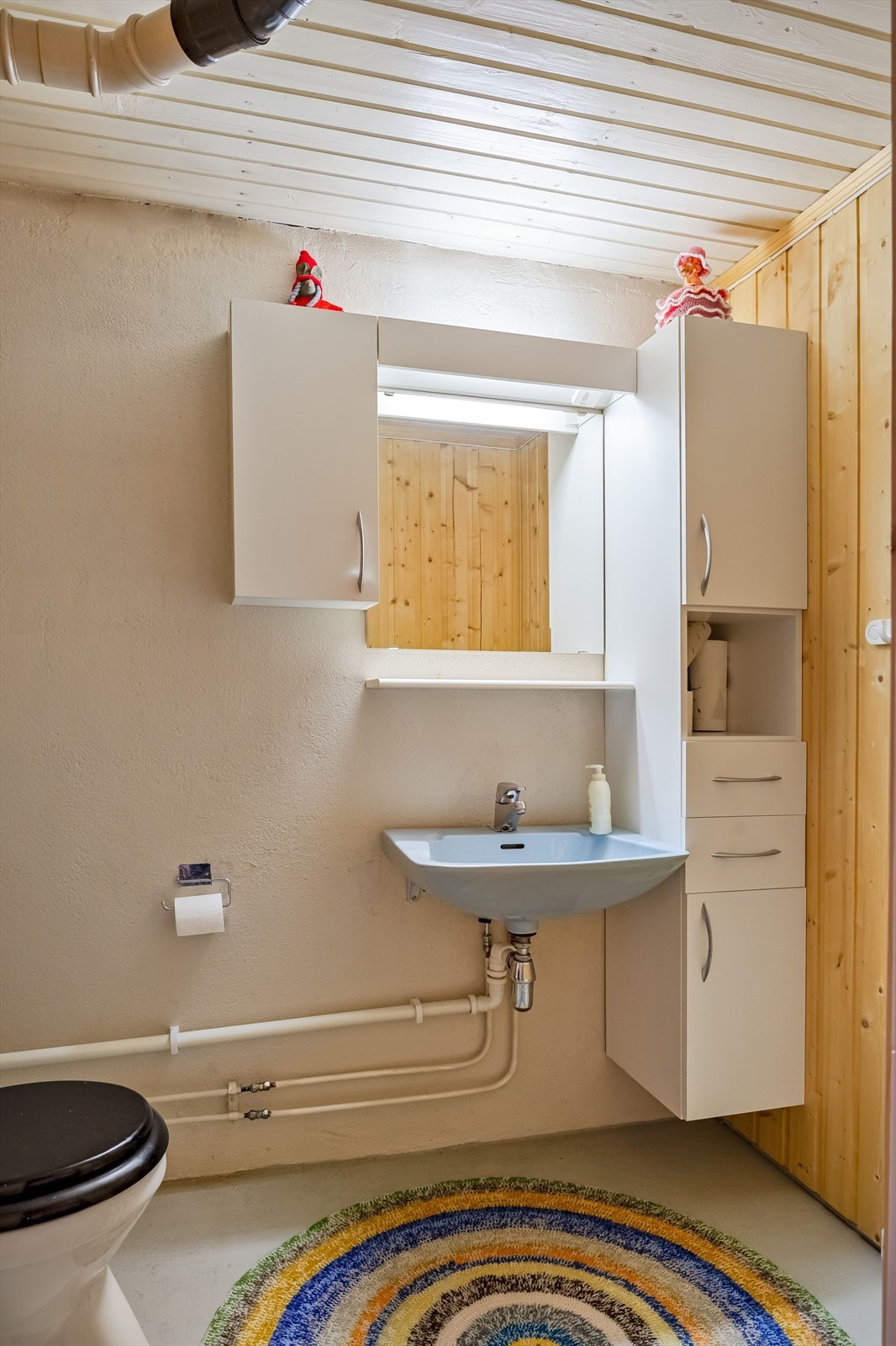 Ekstra toalettrom i kjeller med vinylbelegg på gulv og malt murpuss på veggene. Rommet er utstyrt med vegghengt servant, speil med belysning og vegghengte skap over, samt gulvstående toalett. Galleribilde