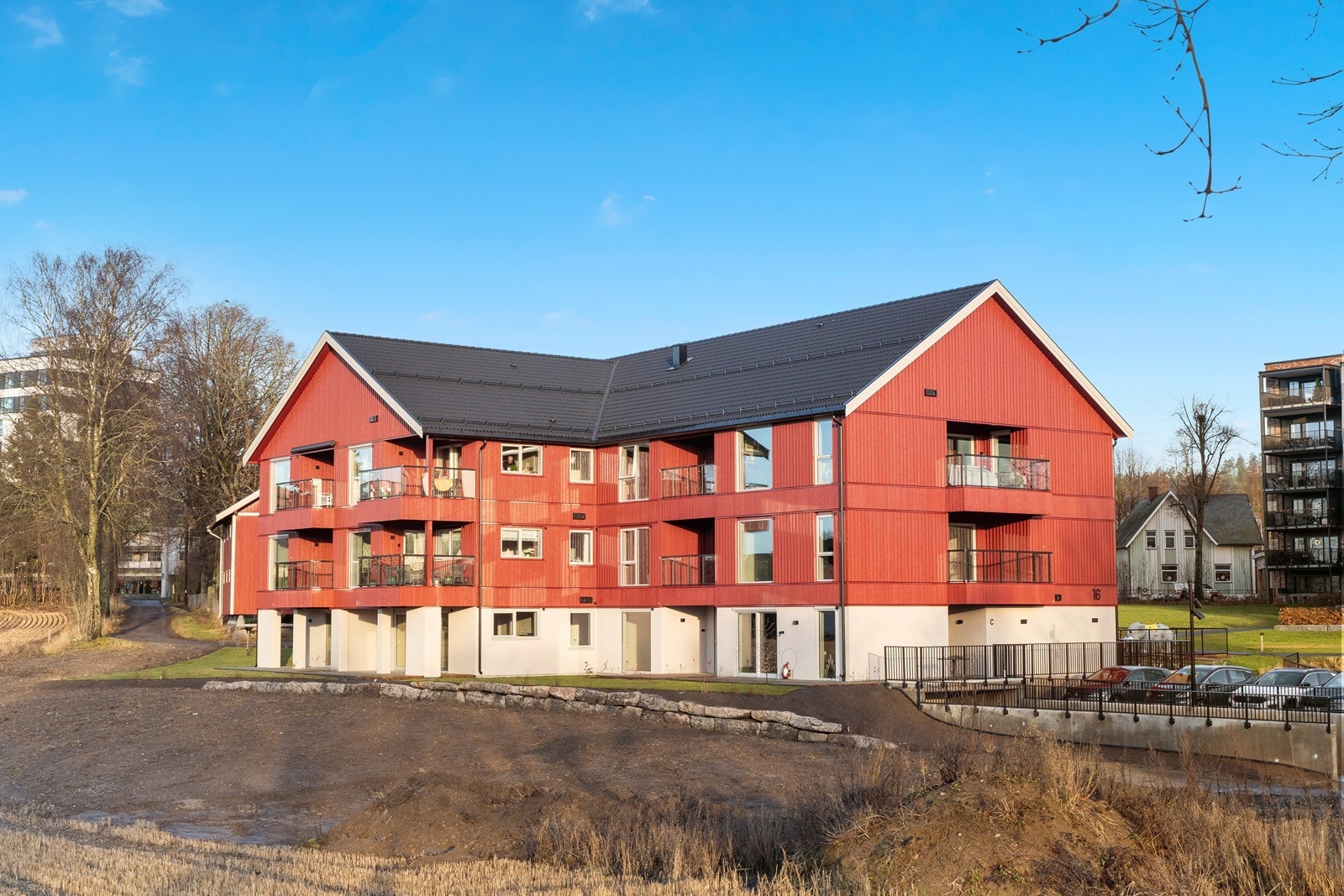 Bygningen har en moderne utforming med stående trekledning i rød utførelse og betongkonstruksjon. Galleribilde