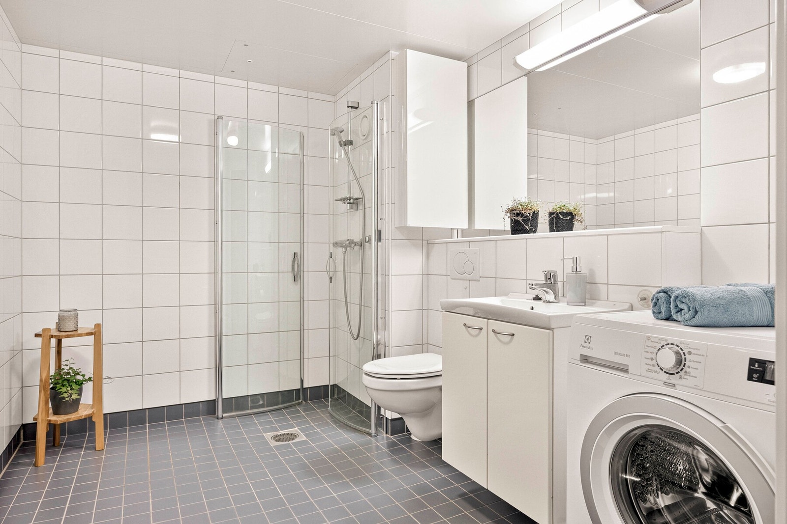 Flislagt bad med varmekabler i gulv - innredet med veggmontert toalett, servant med underskap og speil over. Galleribilde