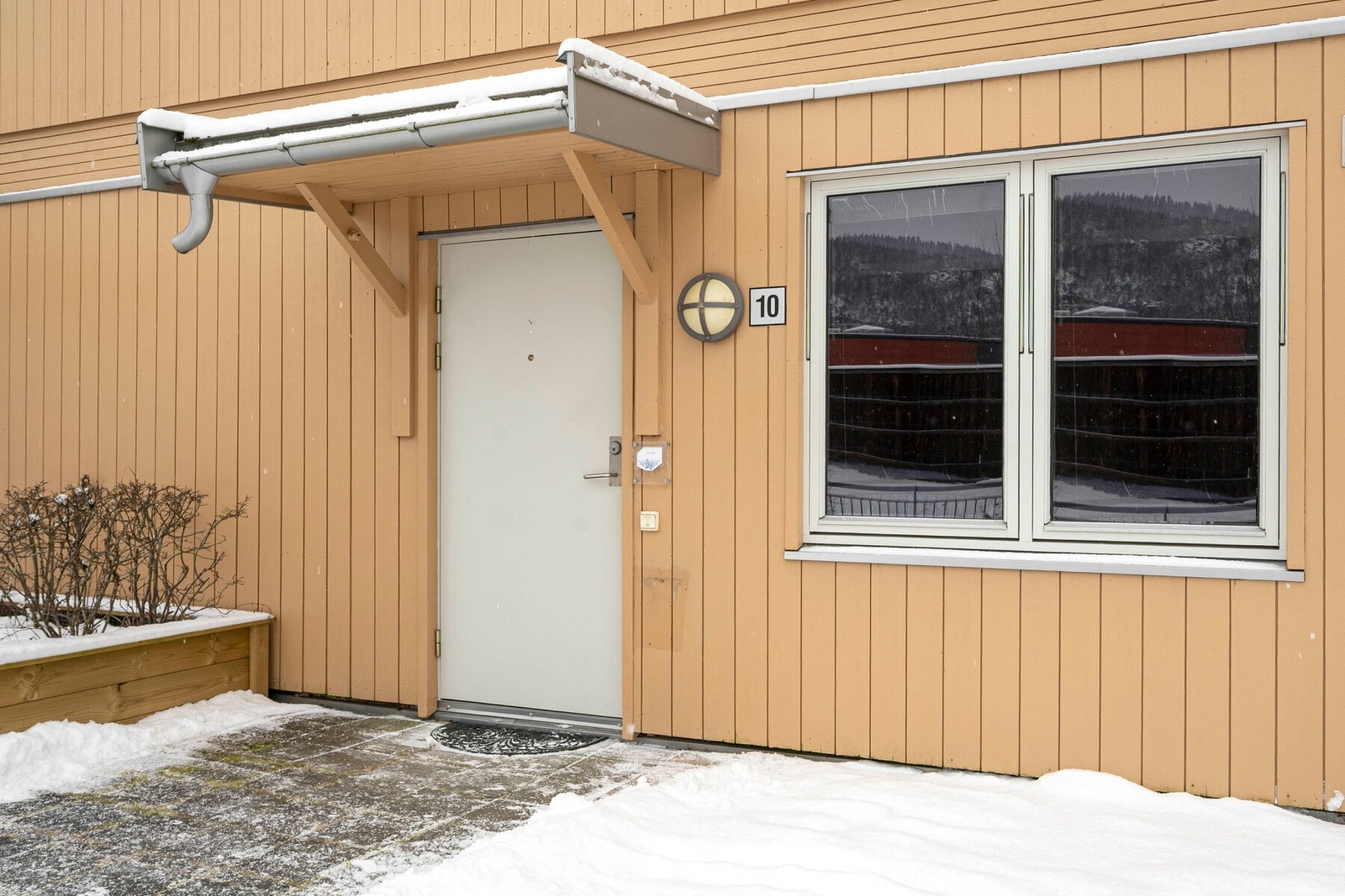 Boligen har eget inngangsparti med et praktisk overbygg som skjermer mot snøen på vinterstid. I sommerhalvåret kan man møblere med en liten sittegruppe for å nyte morgensolen. Galleribilde