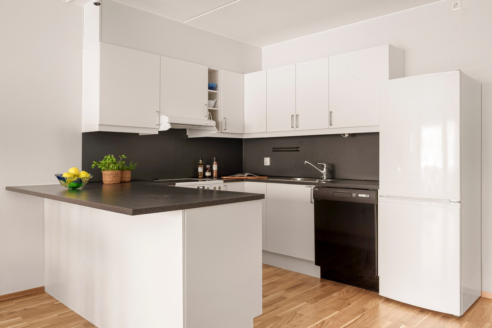 Kjøkken med slette fronter og benkeplate i laminat, utformet med en praktisk halvøy som gir ekstra benkeplass og mulighet for barstoler. Galleribilde