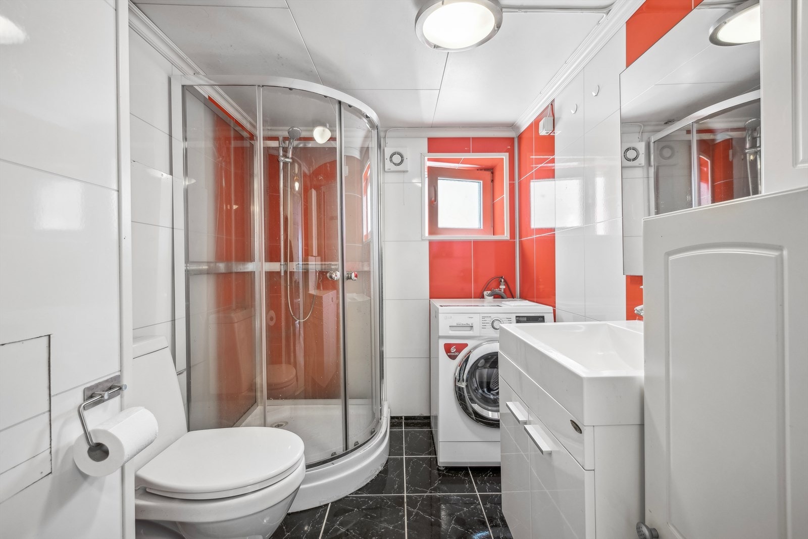 Badet i kjelleretasje er utstyrt med gulvstående klosett, servant på skap, speil, veggskap, dusjkabinett og opplegg for vaskemaskin. Badet er av eldre dato. Selger opplyser at han selv har skiftet fliser på badet i 2015. Galleribilde