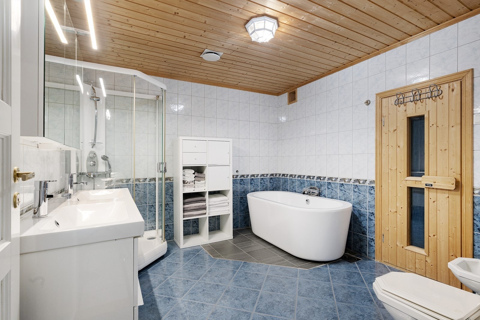 Flislagte vegger og ubehandlet trepanel gir et robust bad med dusjkabinett og badekar. Galleribilde