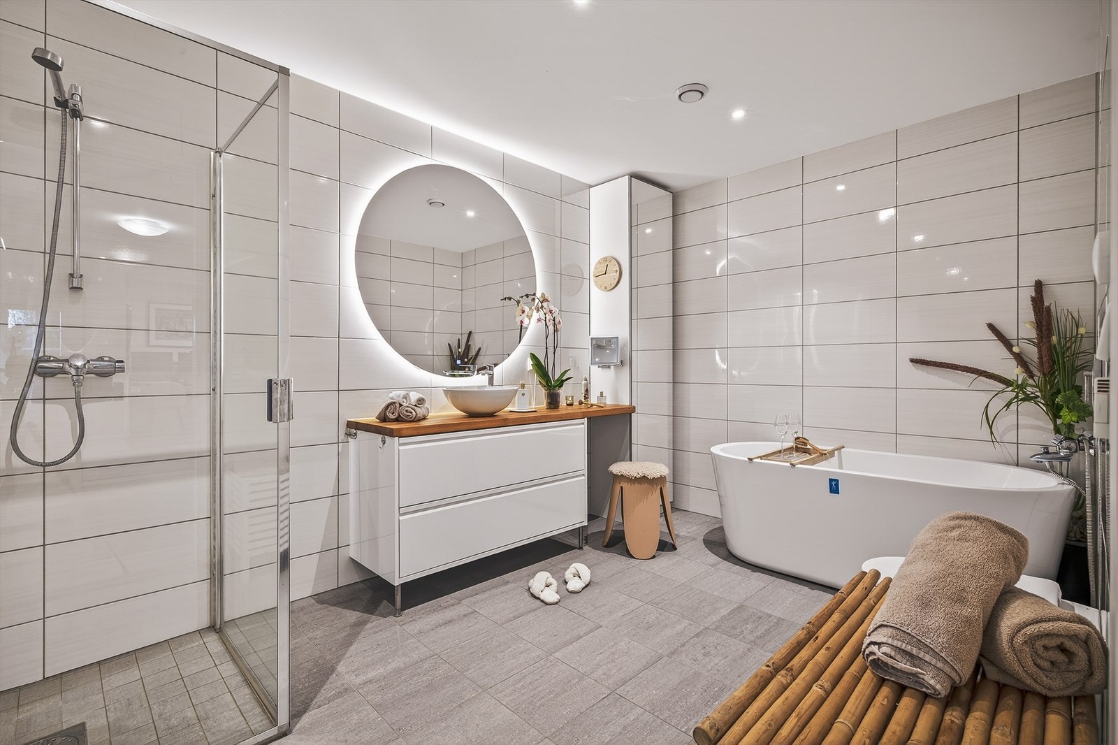 Badet inneholder foldedører i dusj, badekar, vegghengt toalett, og baderomsinnredning med servant og belyst speil. Galleribilde